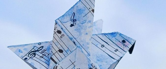 Artistic origami sailboat crafted from sheet music under a bright blue sky.